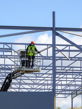 Üniformalı ve çelik iskelet arka planında emniyet koruyucu ekipmanlı otomatik eklemli asansör sepetinde çalışan işçiler