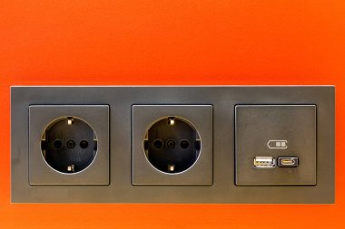 A modern black 220V, USB and USB C socket block is built into the orange wall surface