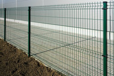 Yeni bir sanayi bölgesinin etrafını çevreleyen yeni yeşil metal parmaklıklar, bir tarafında çimen toprağı ve diğer tarafında asfalt şerit.