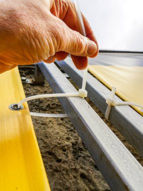 Fastening process of the outdoor vinyl advertising banner to the metal frame with the help of plastic cable ties, billboard fastening to frame