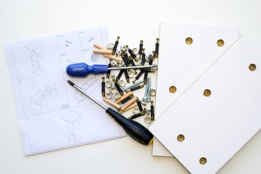 Mobilya donanımı. Yeni bir mobilyanın beyaz kaplamalı yonga parçaları, mobilya montaj şeması üzerine çeşitli montaj malzemelerinin yığını.