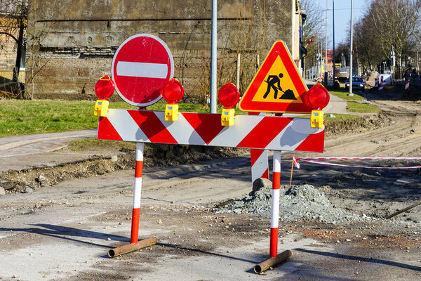 Red and white striped traffic warning barrier with red lights and prohibition signs before street repair site in city