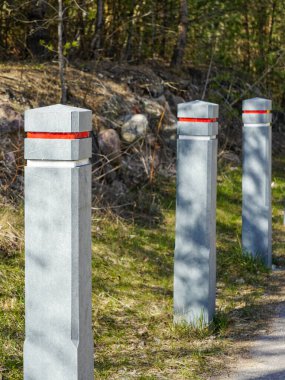 Bir doğa parkında park alanını sınırlamak için kırmızı ve beyaz yansıtıcı bantlı kare beton direkler