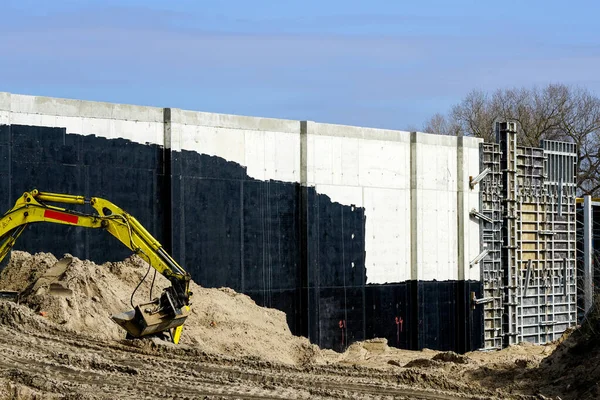 stock image Concrete wall of a huge water reservoir built using concrete formwork, partly covered with black waterproofing sealant and earth