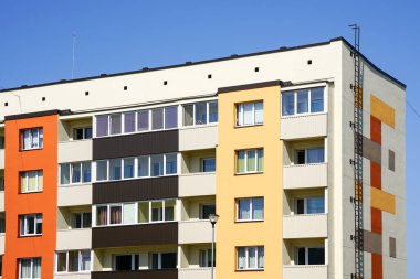 Yenilenmiş ve termal izole edilmiş renkli çok katlı bina ön cephesi merdiveni mavi gökyüzü arka planında.