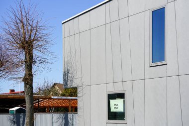 Penceresinde mavi gökyüzü arka planında satılık olduğu yazan yeni modern ev gri cephe parçası.