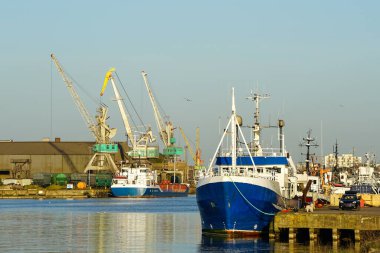 Gün batımında gemi ve vinçlerle liman manzarası, Liepaja, Letonya, Baltık denizi