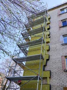 Çok katlı bir apartmanın dış cephesinin termal yalıtımı kalın kaya mineral yünü döşemeleri, iskele, mavi gökyüzü arka planı