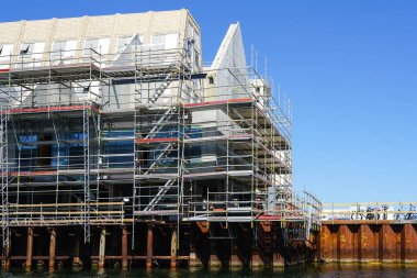 Metal yığınları üzerine inşa edilmiş bir evin yeniden inşa çalışmaları ve suyun kenarındaki çelik kaburga duvarı, ön cephenin iskelesi, Kopenhag, Danimarka