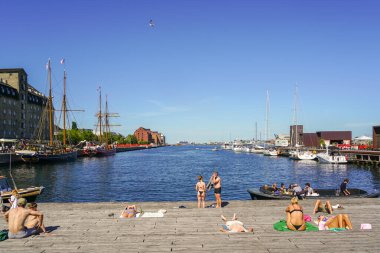 Kopenhag, Danimarka - 30 Mayıs 2023: İnsanlar güneşli bir günde şehir merkezindeki rıhtımdaki ahşap bir terasta dinlenirler.