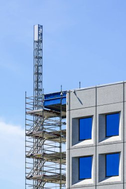 Geçici asansör platformu, mavi gökyüzü arkaplanı ve taşınabilir iskelesi olan modern bir ofis binasının onarımı.