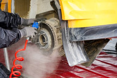 Servis parkında araba bakımı, fren diski ve kalibre tozunu sıkıştırılmış hava ile havaya uçurmak.