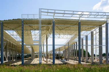 Güçlendirilmiş beton destekli çelik çatılı, mavi gökyüzü arka planlı, tamamlanmamış yeni bir çelik yapı.