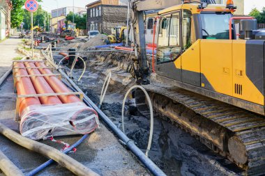 Street reconstruction view, deep and wide trench, replaced underground pipes and wells, new pipes, excavator, dewatring system pipes and hoses clipart