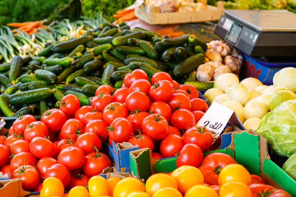 Various colorful fresh and organic vegetables at a farmers market, red and yellow tomatoes, cucumbers, onions, carrots, cabbage