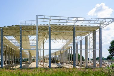 Güçlendirilmiş beton destekli çelik çatılı, mavi gökyüzü arka planlı, tamamlanmamış yeni bir çelik yapı.