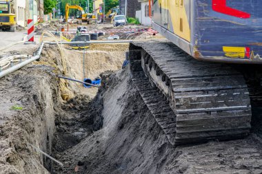 Derin hendeğin yanında ağır sürüngen kazıcısı, sokak yeniden inşa manzarası, kanalizasyon ve su boruları, plastik denetim kuyuları