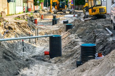 Geniş bir siper, kanalizasyon ve su boruları ve birçok plastik denetim kuyusu ile sokak yeniden inşa manzarası