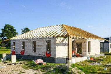 Beyaz beton blok duvarları ve ahşap kiriş kiriş çatı yapısı, mavi gökyüzü arka planı olan bitmemiş bir ev.