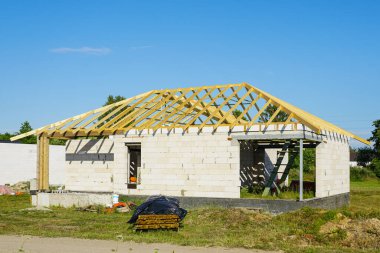 Beyaz beton blok duvarları ve ahşap kiriş kiriş çatı yapısı, mavi gökyüzü arka planı olan bitmemiş bir ev.