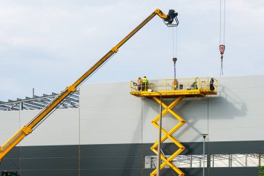 Sandviç panelleri duvar montajını teleskopik bumlu vinç ve sarı kendinden itişli makas kaldırma platformu kullanarak yapar