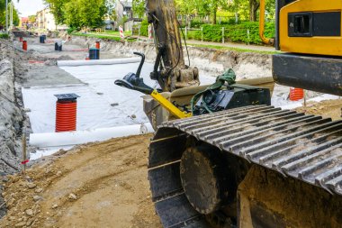 Sokakların yeniden inşasında drenaj ve temel katmanların ayrılması için jeotextile kumaş rulo kullanımı, ön planda sürüngen kazıcı