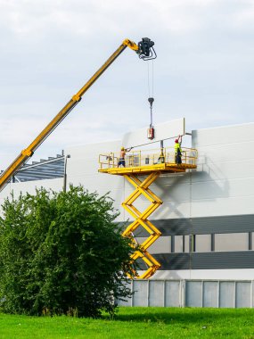 Sandviç panelleri duvar montajını teleskopik bumlu vinç ve sarı kendinden itişli makas kaldırma platformu kullanarak yapar