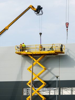Sandviç panelleri duvar montajını teleskopik bumlu vinç ve sarı kendinden itişli makas kaldırma platformu kullanarak yapar