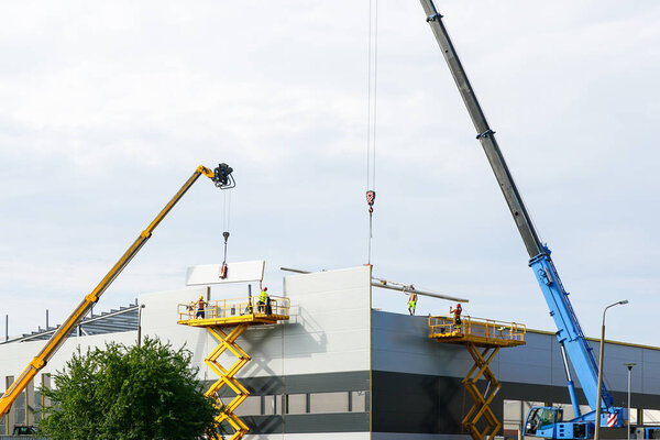 Assembly of sandwich panel walls and roof using two telescopic jib cranes and two self propelled scissor lifts