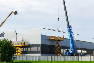 Sandviç paneli duvarları ve çatısı iki teleskopik flok vinç ve iki kendinden itişli makas kaldıracı kullanarak monte edildi.