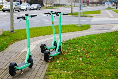 Üç yeşil kiralık elektrikli scooter şehir sokaklarında müşterileri bekliyor. Park edilmiş elektrikli scooterlar, kentsel hareketlilik...