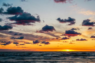 Baltık Denizi kıyısında çok renkli altın bir gün batımı, deniz kıyısında çok renkli altın bir gün batımı, koyu tüylü kümülüs bulutları.