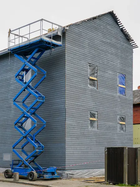 A blue mobile self propelled scissor lift platform raised high next to the grey facade of a residential building