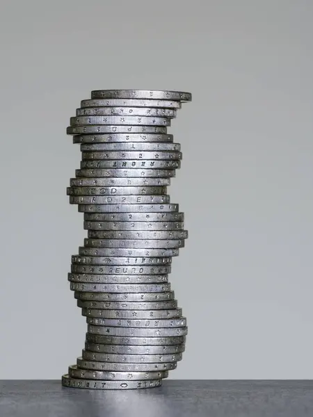 Vertical unstable curved stack of two euro coins on a grey background, unstable coins stack, future instability concept