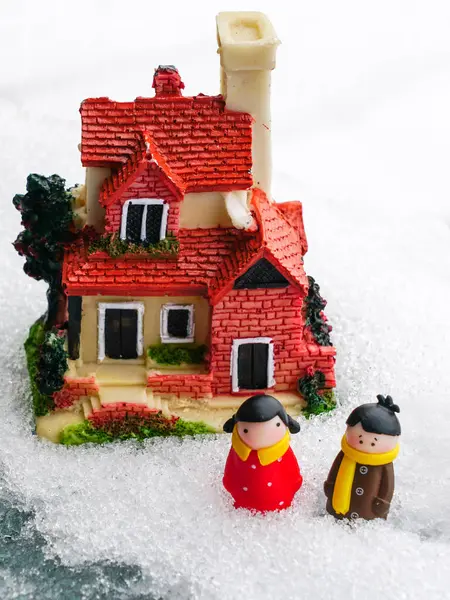 Miniature figures of a man and a woman in the snow near a miniature residential house, house cost concept
