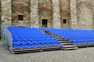 Outdoor concert hall with empty blue rows of seats, mobile metal structure with blue plastic seats in the courtyard of a historic castle clipart