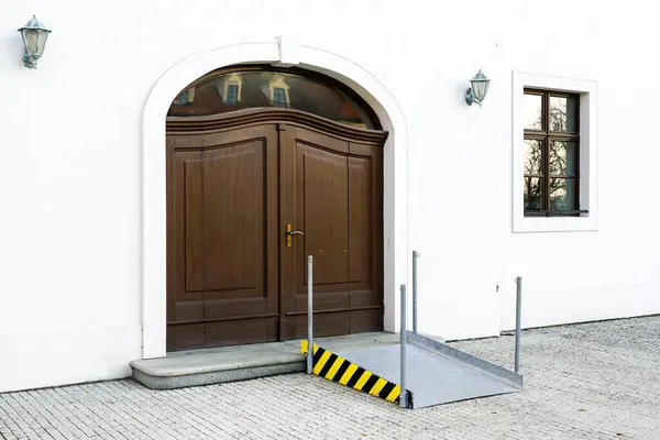 A compact metal wheelchair ramp at the entrance door of a public historic building, entrance suitable for the disabled, one step ramp