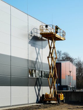 Yüksek sarı kendinden itişli makas kaldırma platformu endüstriyel yapı duvarı teftişi için çalışan işçilerle birlikte, mavi gökyüzü arka planı