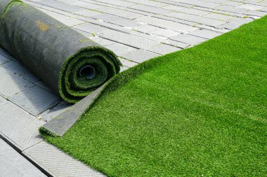 Preparing artificial green grass carpet rolls for outdoor event flooring in the town square clipart