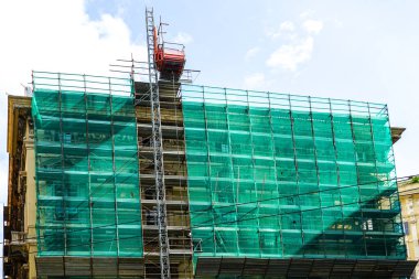 Yeşil güvenlik ağıyla kaplanmış prefabrik metal tüp iskelesi ve kaldırma malzemeleri için elektrikli asansör kullanılarak tarihi bina cephesi yenilenmesi