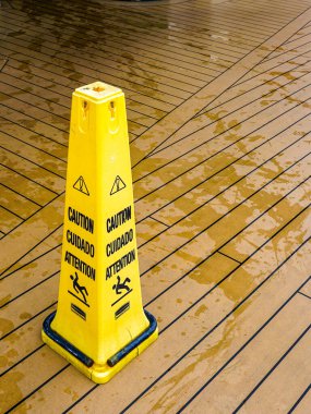 A yellow plastic warning pylon about the slippery wet floor on the deck of a cruise ship, safety cone wet floor, caution wet floor clipart