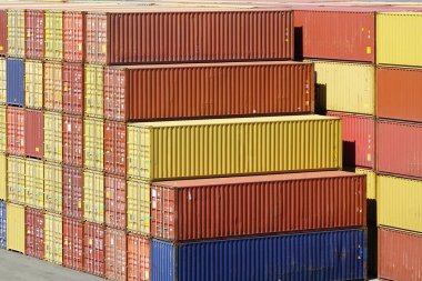 Sarı, turuncu, kırmızı ve mavi nakliye konteynırları liman terminalinde çeşitli katmanlarda istiflenmiş konteynırlar.