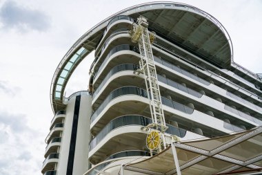 Geminin yüksek kıç tarafında cam parmaklıklı kamaraları, arka planda balkonları ve gemi gövdesi yıkama tesisi olan lüks bir yolcu gemisi var.