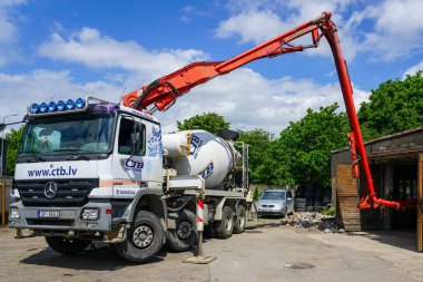 Liepaja, Letonya - Haziran 06, 2024: Geniş kollu ve hortumlu modern mobil karıştırıcı kamyon pompası kullanarak kapalı alanlara taze beton dökme