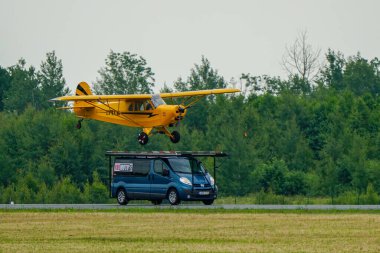 Liepaja, Latvia- June 16, 2024: Risky and dangerous stunt, a small plane tries to land on the roof of a minibus, stunt pilot lands plane on a minibus clipart