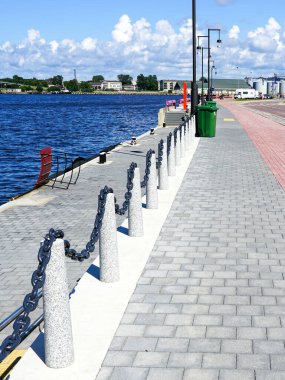 Ventspils, Letonya - Ağustos 03.2024: Şehir güvertesi, limanı çevreleyen metal bir zincir ile birbirine bağlı beton direkler