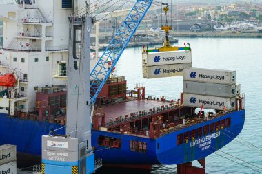 Civitavecchia, Italy- May 29, 2024: Port crane places Hapag-Lloyd cargo containers on board container ship Livorno Express, IMO 9610157 clipart