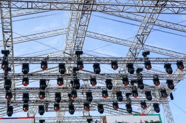 Büyük bir açık hava sahnesinin metal kirişleri ve aydınlatma elementleri, alüminyum konser sahne iskeleti parçaları, sahne ışıklandırması bir kirişe kelepçelenmiş.