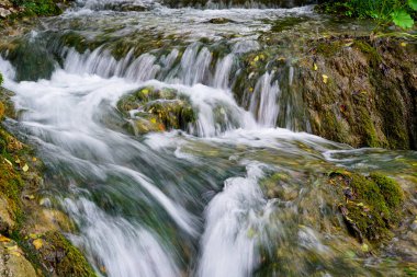 UNESCO Plitvice gölleri, akan su, yeşil doğa arka planındaki yürüyüş yolundan güzel şelalenin düşük çekim hızı.