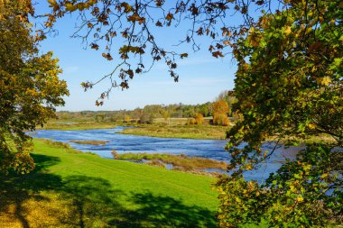 Beautiful scenic Latvian autumn nature landscape, river Venta flows between fields and forests near Kuldiga, picturesque autumnal nature landscape clipart